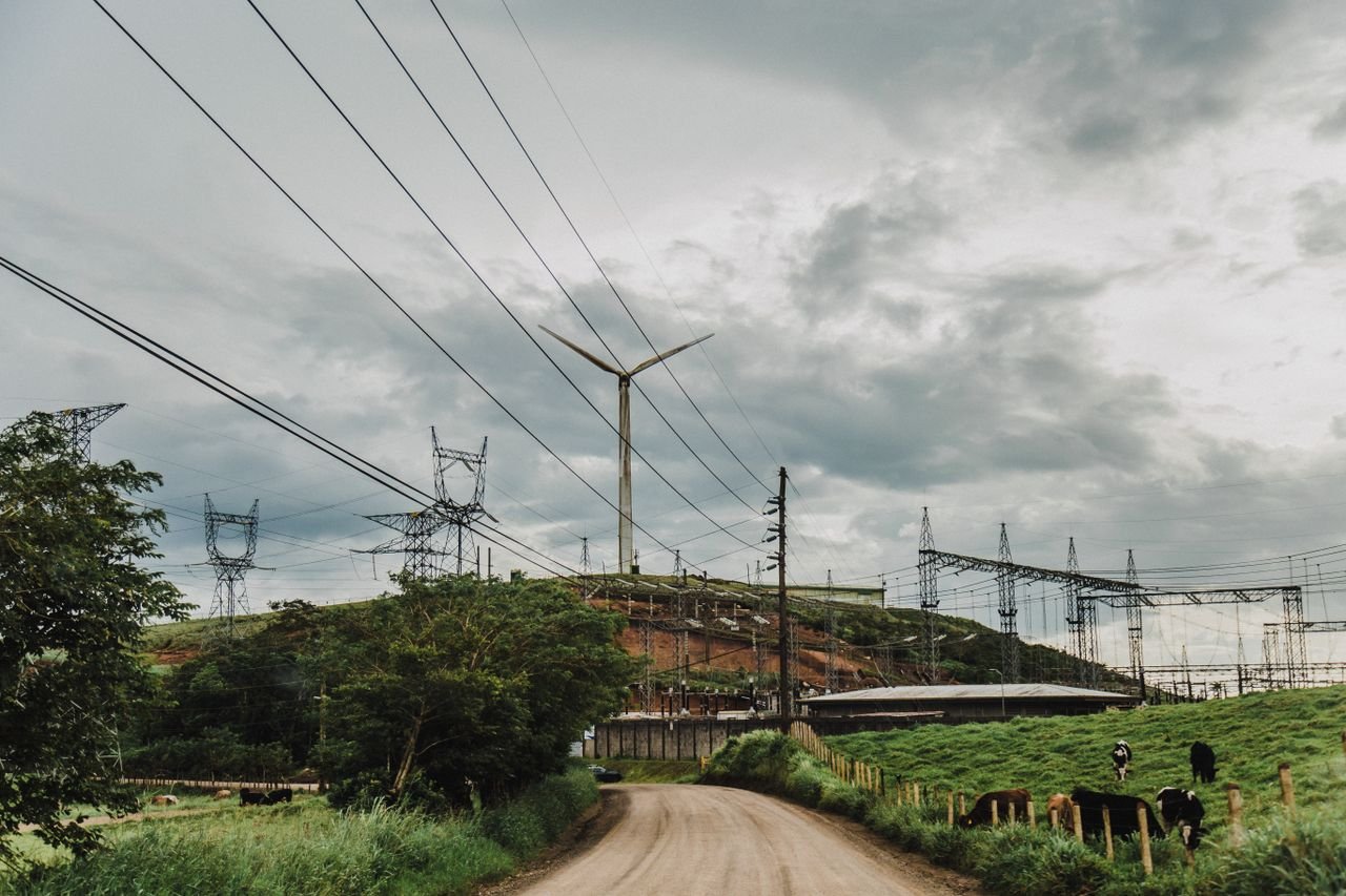 Industrias Serene countryside scene with a wind turbine near power lines and cows grazing.