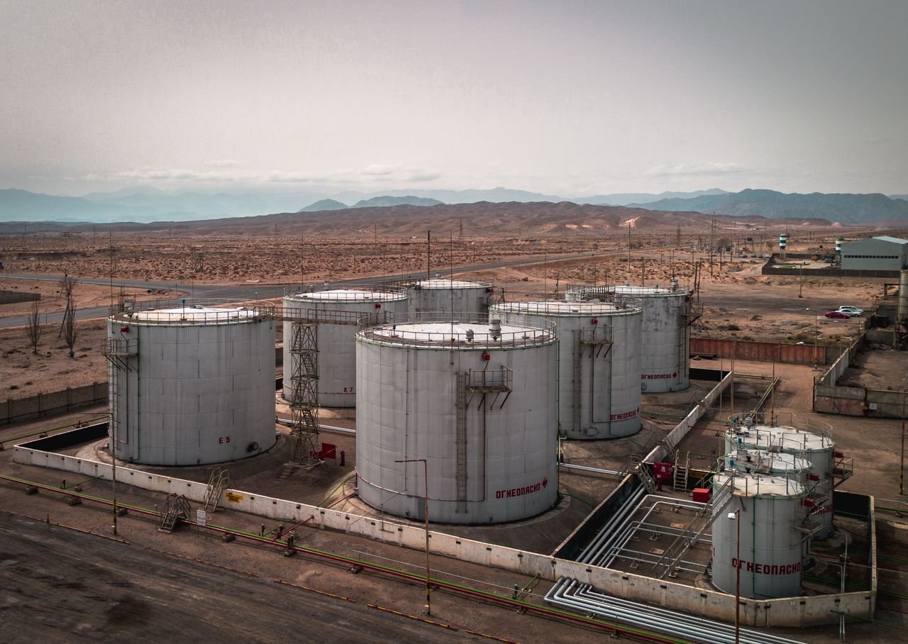 Industrias Aerial view of large industrial oil tanks in a desert setting with mountains in the distance.