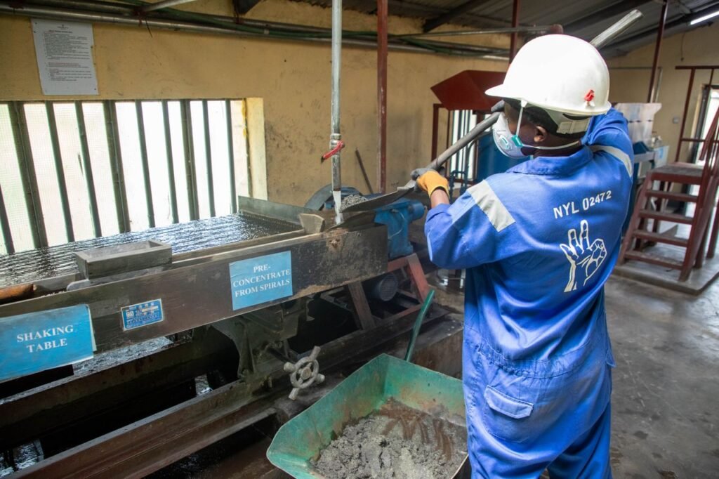 A factory worker in blue overalls operates a shaking table for ore processing.